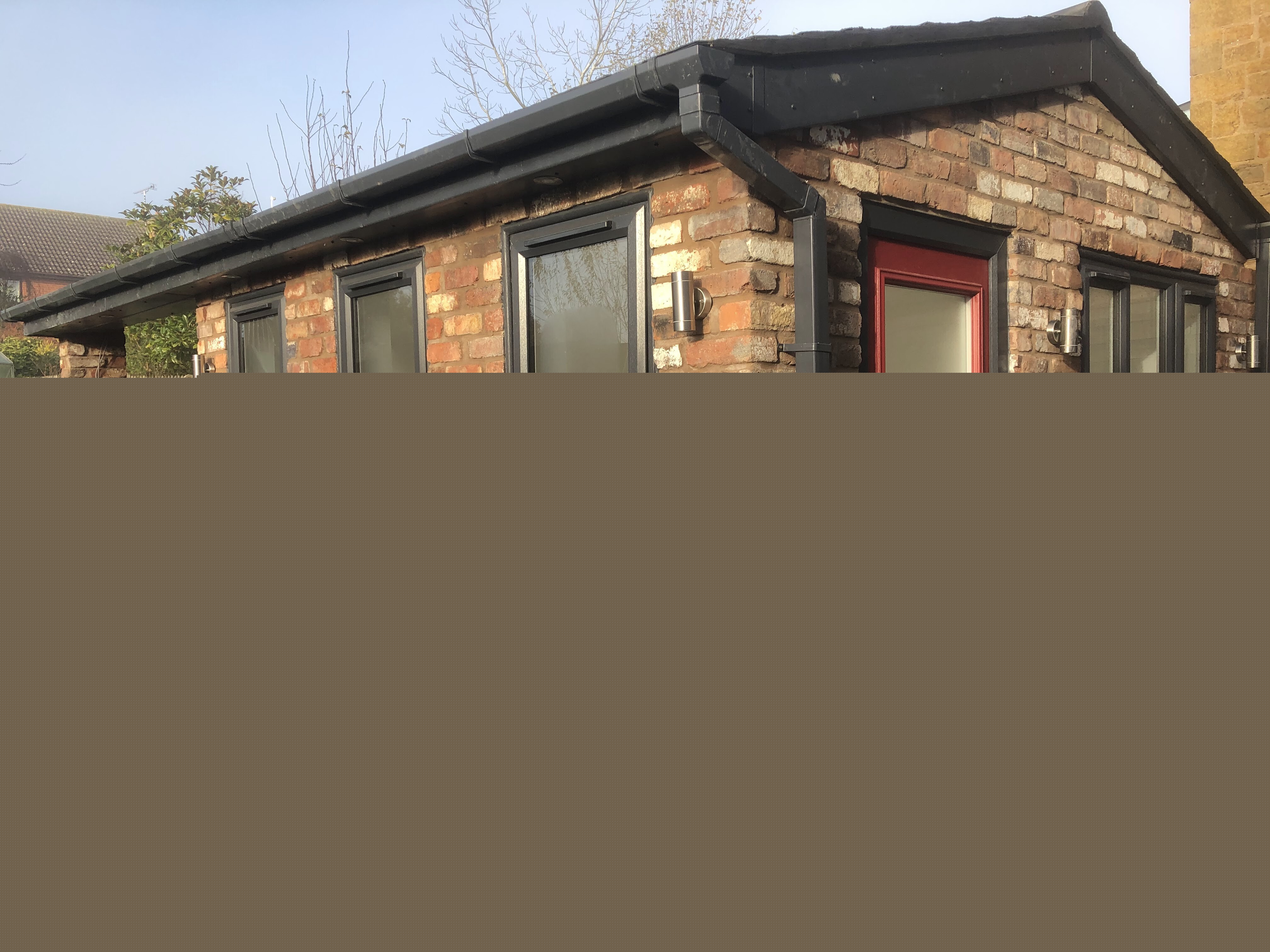 Completed brick-built garden room with tall dark-framed windows and a red entrance door