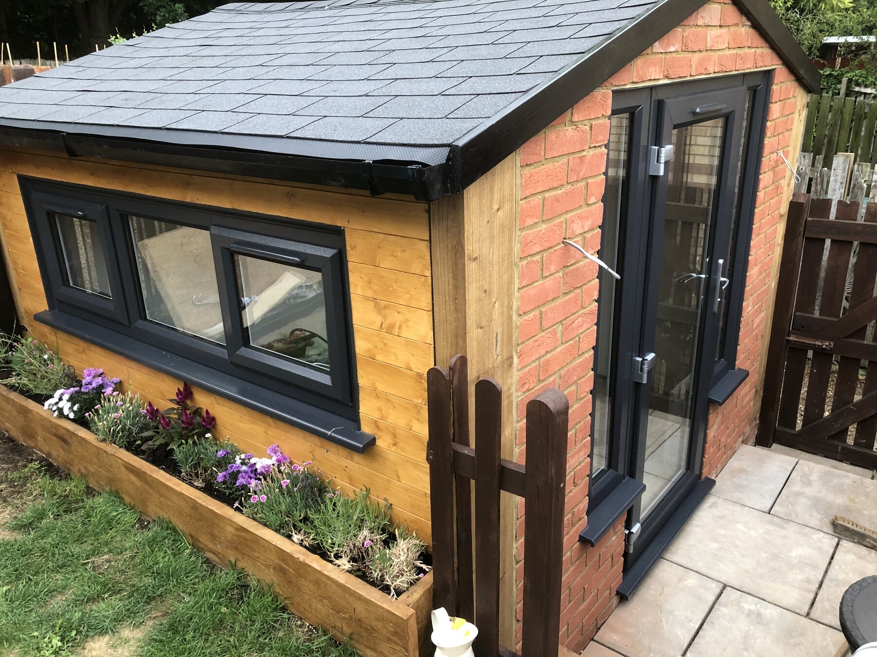 Completed garden room with timber cladding, brickwork, dark-framed windows and glazed double doors